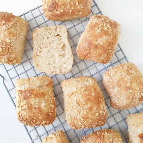 German bread rolls 'Oatys' baked on rack with one cut open for crumb - by BREADISTA