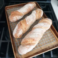 3 baked loaves named Wurzelbrot on a rack - by BREADISTA