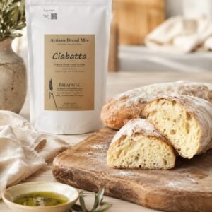 baked Ciabatta loaf, cut in half, faces towards camera on wooden cutting board, dip bowl with olive oil, white bag of BREADISTA bread mix - light kitchen background