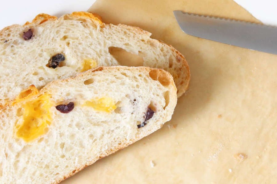 two slice of a mediterranean ciabatta loaf with cheese and black olives on parchment paper - BREADISTA