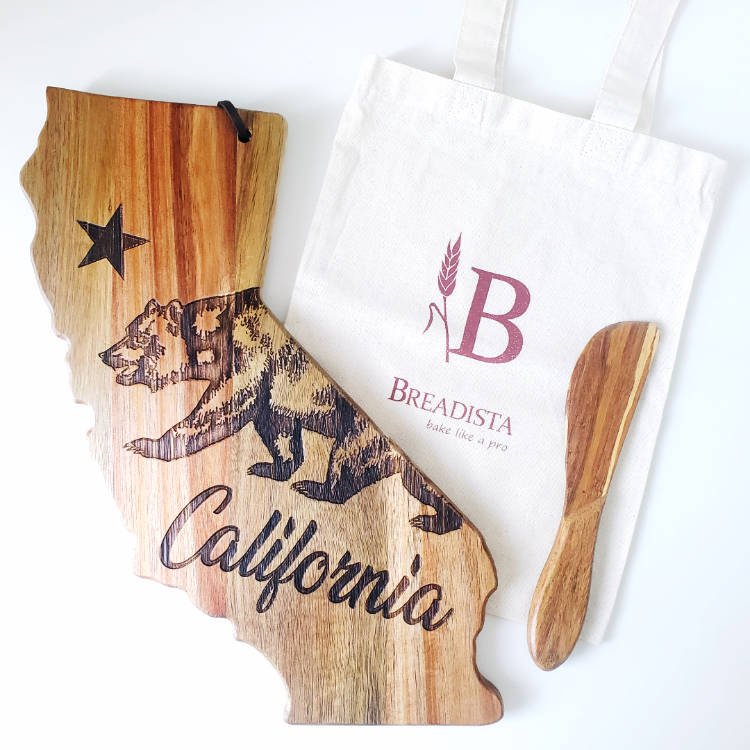 California shaped wooden cutting board with wooden spreader on tote bag with BREADISTA Logo