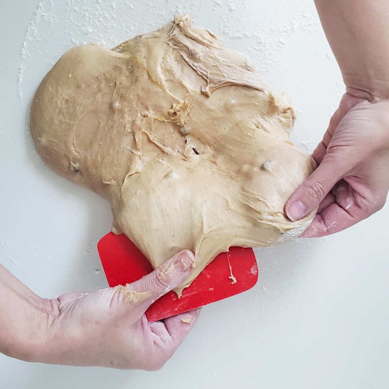 Birdview - two hands hold sticky Colomba dough at the edge ready to be fold