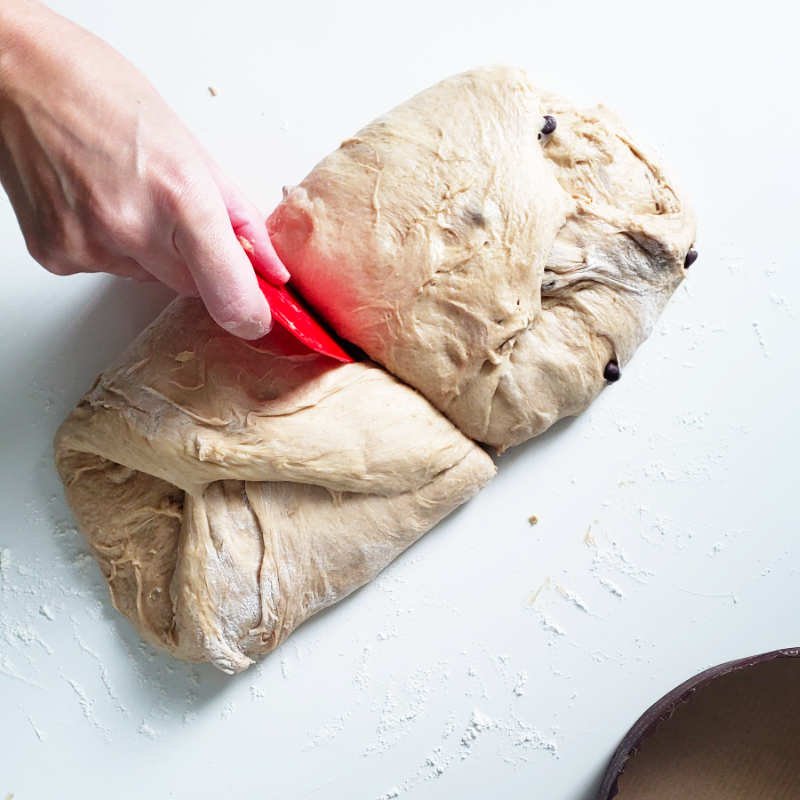 Birdview - dough on counter folded and hand with read dough scraper cuts in half by BREADISTA