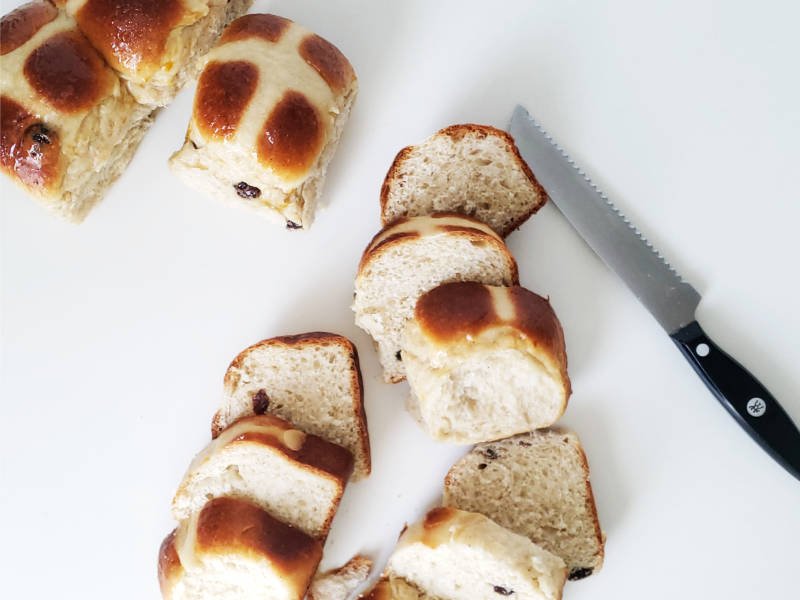 birdview - slices of hot cross buns with serrated knife and whole buns in upper left corner