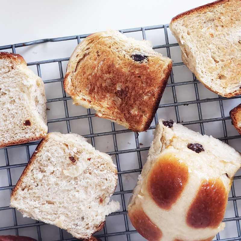 birdview - slices of toasted and untoasted hot cross buns with one whole bun next to it on rack by Breadista