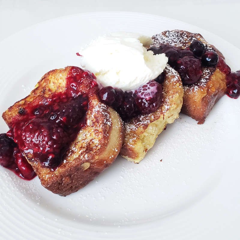 closeup - white plate served with 3 slices of brioche french toast with mixed berry compote topped with scoop of vanilla ice-cream by BREADISTA