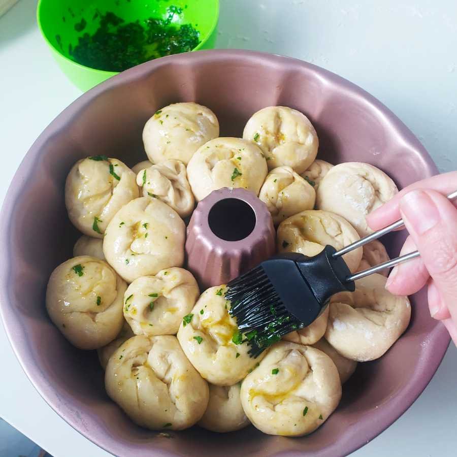 birdview - round dough pieces layered in bundt pan get brush by hand with garlic oil - BREADISTA