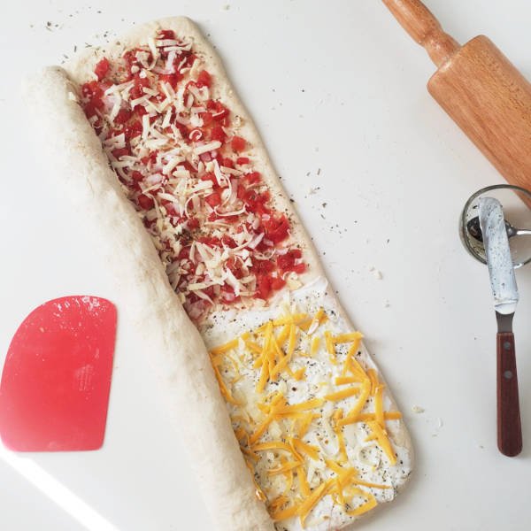 rolled out dough topped with pizza items - half way rolled up on counter top - BREADISTA