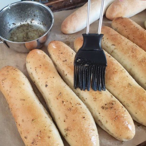 homemade Breadsticks baked, getting brushed with melted herb butter on sheet - by BREADISTA