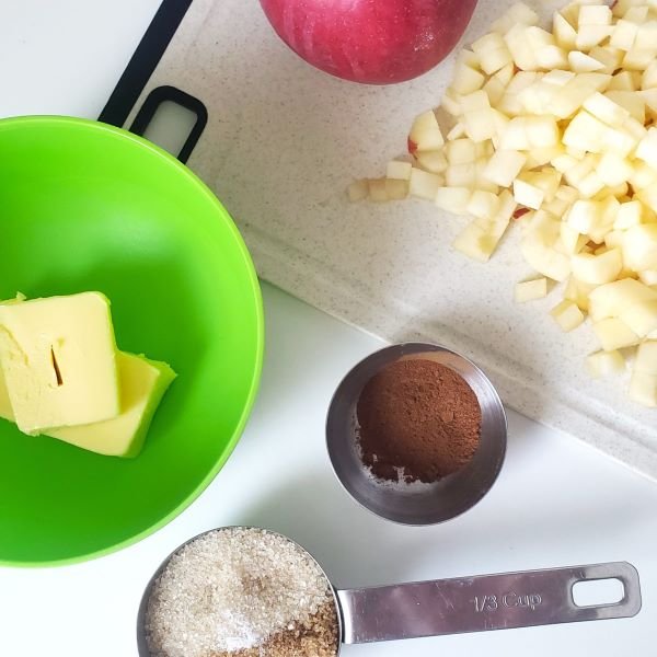 birdview - prepared ingredients for cinnamon rolls: diced apples, third of cup with mixed sugars, butter in green bowl, cinnamon in metal cup - by BREADISTA