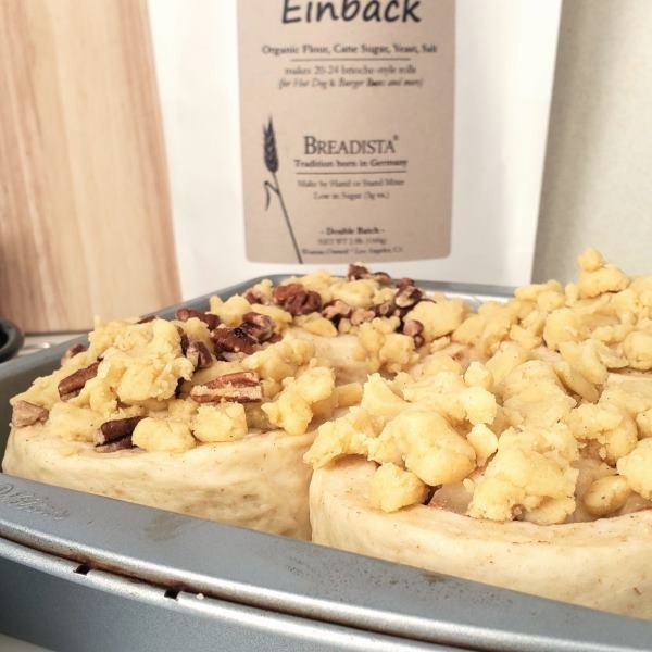 tight closeup - big unbaked but proofed raw apple-cinnamon rolls with streusel-nut topping in pan, bread mix EINBACK in the blurry background - by BREADISTA