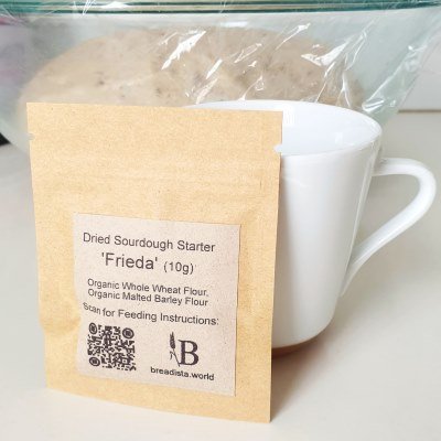 'Frieda' - brown small zip kraft paper bag of 10g dried sourdough flakes leaning at espresso cup - BREADISTA