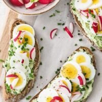 open faced dark artisan bread slices with avocado mash, egg slices, red radishes and chive - NL
