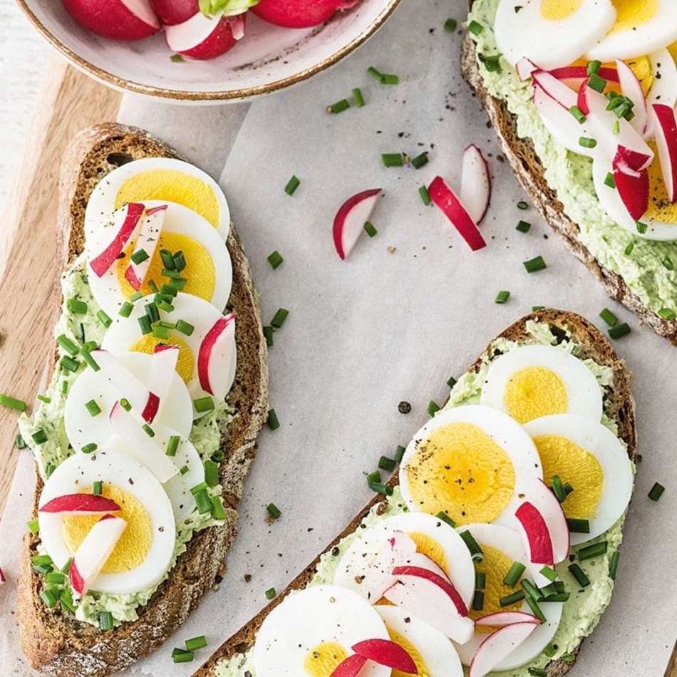 open faced dark artisan bread slices with avocado mash, egg slices, red radishes and chive - NL